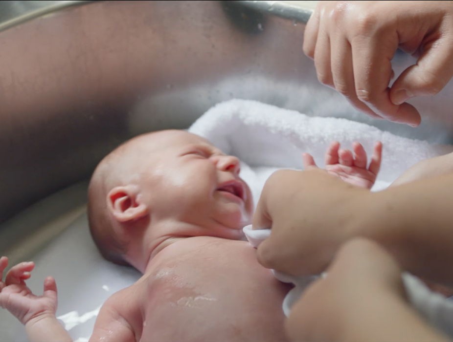 A parent bathing their infant in a sink